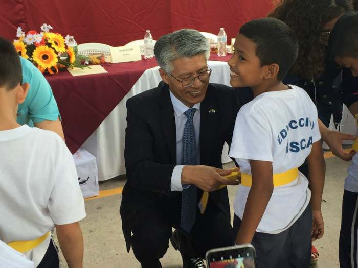 Embajador Shin Seung-ki, coloca la cinta a uno de los niños participantes en el programa que responde con una sonrisa.